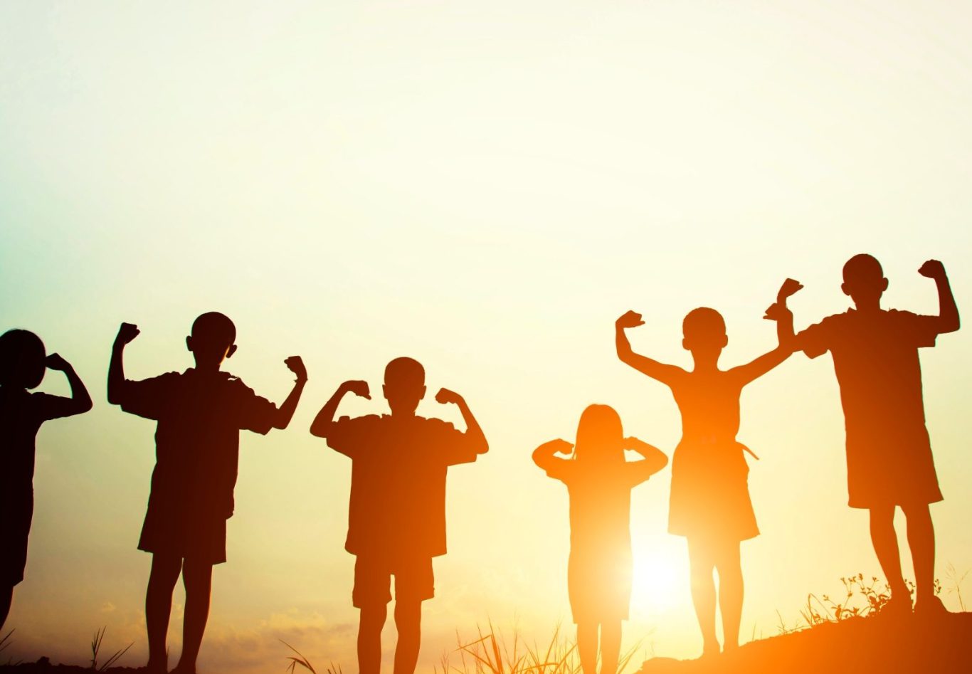 Silhouetten von Kindern, die stolz ihre Muskeln unter einem Sonnenuntergang zeigen.