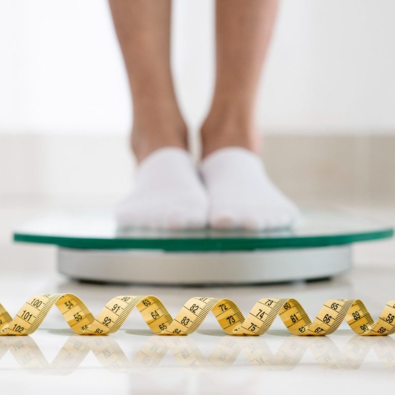 Junge Frau mit rotbraunen Haaren hält sich den Kopf und schaut sorgenvoll auf ein Buch in der Hand.