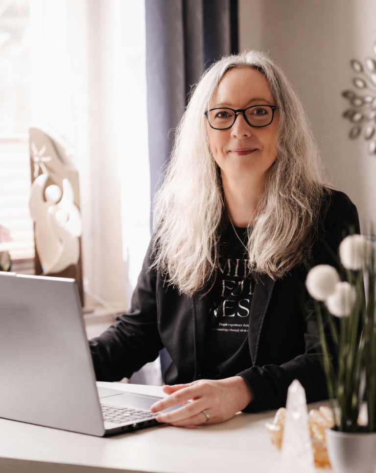 Anett Bartelt Hypnosetherapeutin Frau lächelt vor grünem, blättrigem Hintergrund.