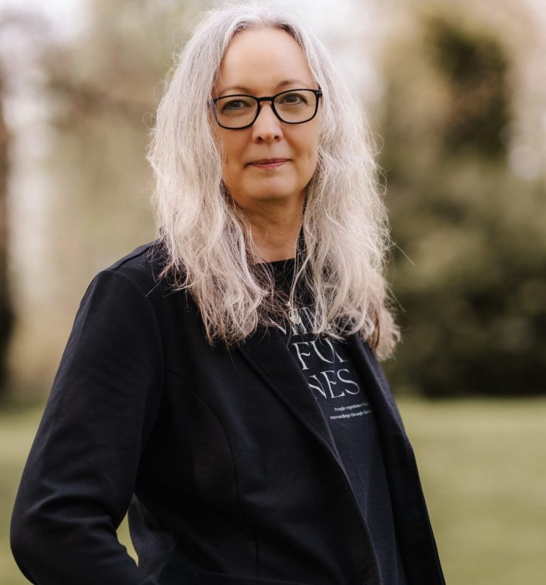 Frau lächelt vor grünem, blättrigem Hintergrund.